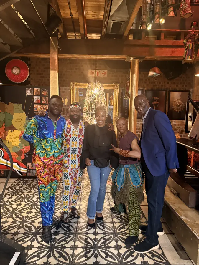 Five people pose together at eat-mea-2025 event in a vibrant African-themed venue; some wearing colorful traditional attire.