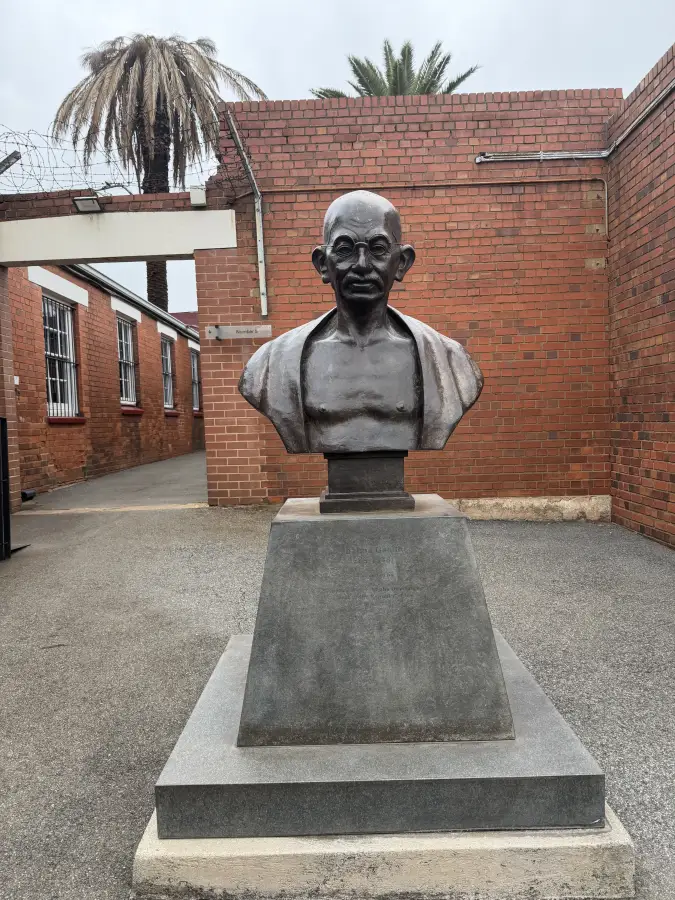 Bronze bust of Mahatma Gandhi on a stone pedestal in a brick courtyard; eat-mea-2026 heritage site visit.