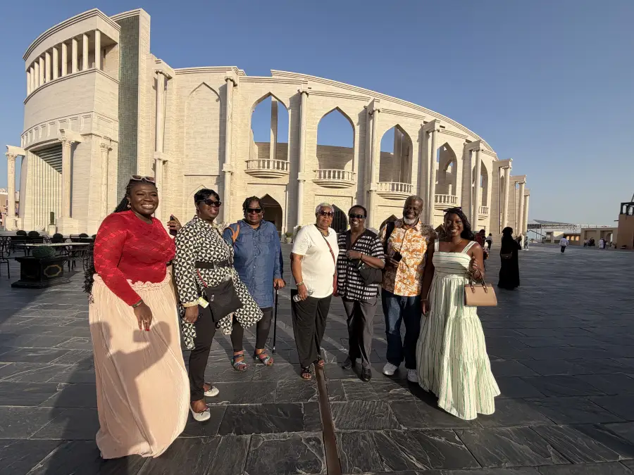 Seven travelers pose before a grand arched limestone building during the EAT MEA 2026 tour in Qatar.