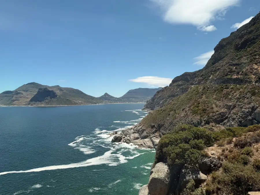Dramatic rocky cliffs overlooking Hout Bay's turquoise waters with mountain backdrop; captured for eat-mea-2026 travel sho