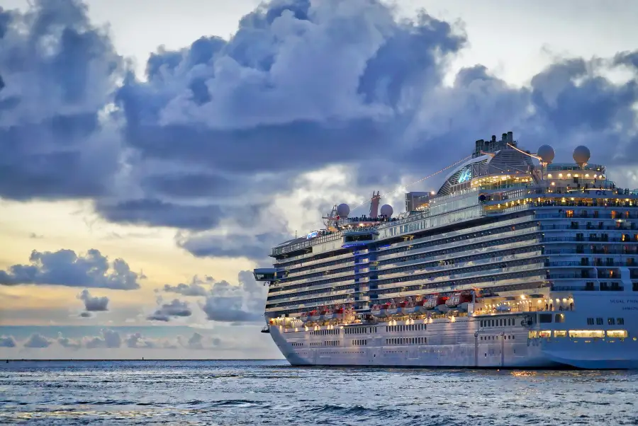Regal Princess cruise ship illuminated at dusk; sailing calm ocean waters under dramatic cloudy sky.