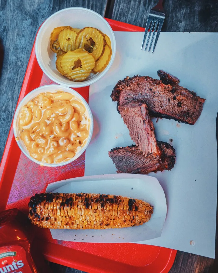 A Southern soul food and barbecue plate with smoked brisket, macaroni and cheese, and grilled corn served on a red tray