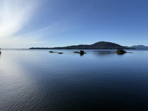 Calm blue waterway with small forested islets and a tree-covered hill in Alaska-Sitka's scenic island archipelago under cl