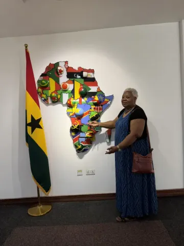 Woman pointing to Africa wall map with national flags beside Ghana flag at eat-mea-2026 event venue.