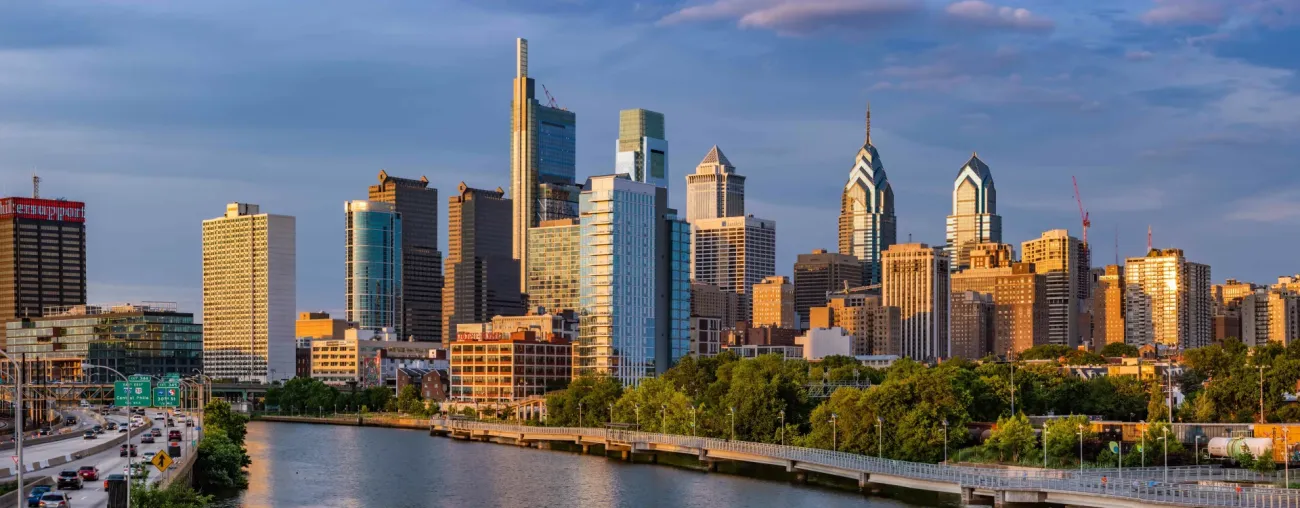 Philadelphia Pennsylvania downtown skyline at golden hour viewed across the Schuylkill River with highways and lush trees