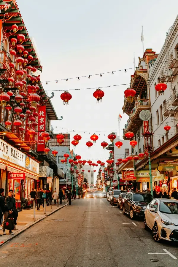 Red lanterns line Grant Avenue in San Francisco; CA's Chinatown; with shops and pedestrians along a vibrant street at dusk.