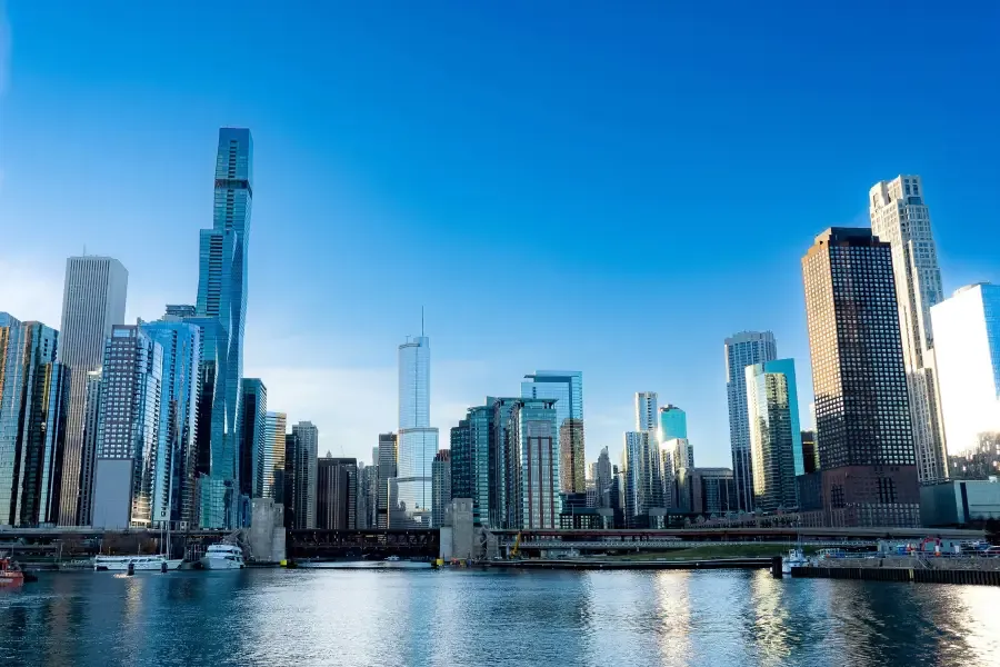 Chicago downtown skyline with glass skyscrapers reflecting over the Chicago River on a clear blue-sky day.
