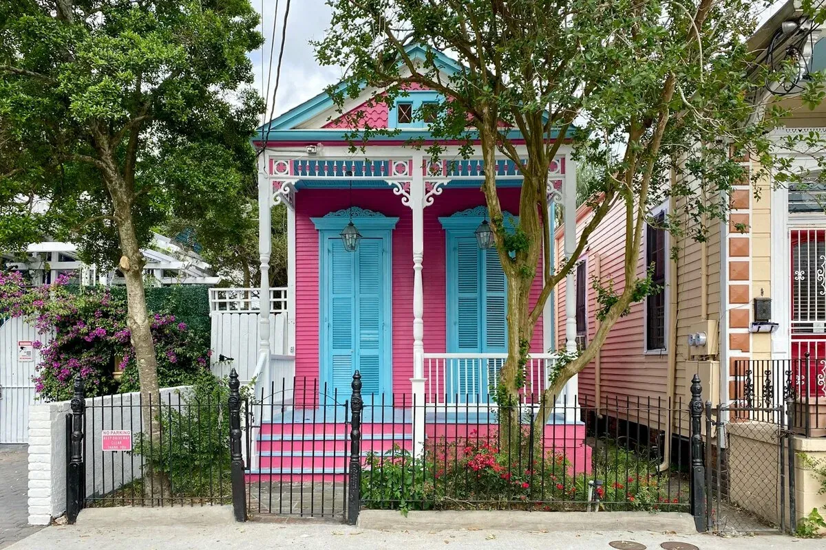 A brightly painted pink and blue Creole cottage with ornate gingerbread trim and a picket fence in a historic New Orleans neighborhood