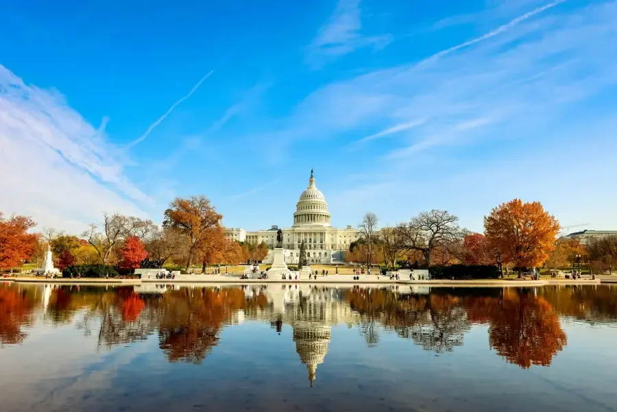 US Capitol building reflected in the Capitol Reflecting Pool surrounded by autumn foliage in Washington; DC on a clear day.