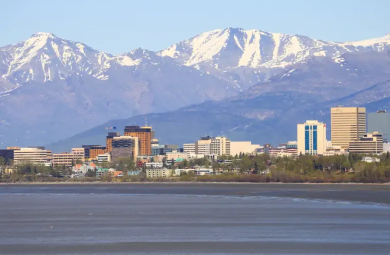 Anchorage; Alaska downtown skyline with snow-capped Chugach Mountains behind and Cook Inlet waters in foreground.