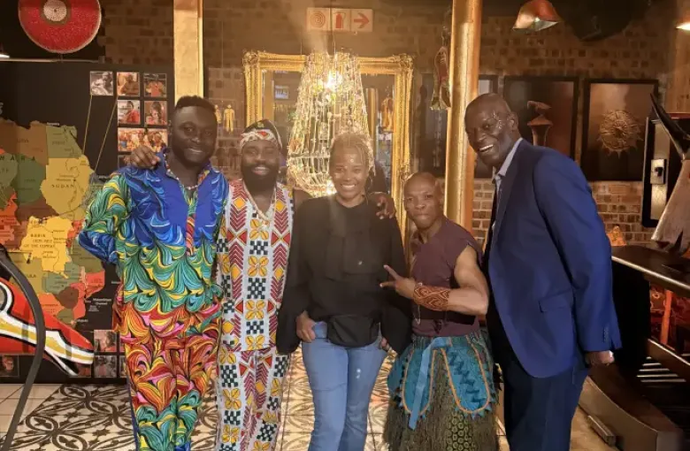 Five people pose together at eat-mea-2025 event in a vibrant African-themed venue; some wearing colorful traditional attire.
