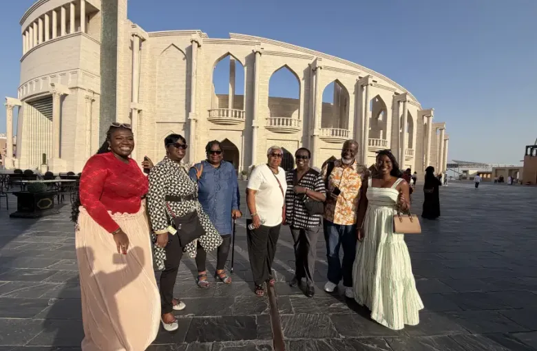 Seven travelers pose before a grand arched limestone building during the EAT MEA 2026 tour in Qatar.