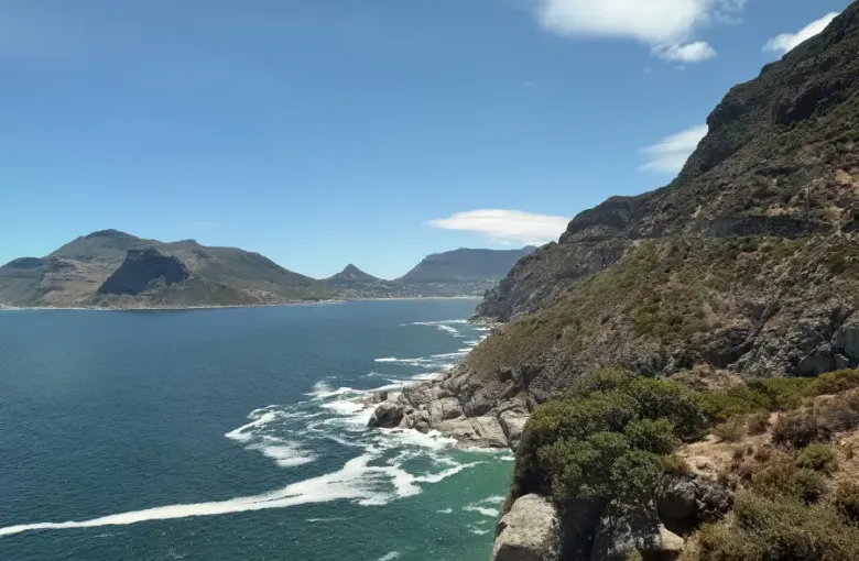 Dramatic rocky cliffs overlooking Hout Bay's turquoise waters with mountain backdrop; captured for eat-mea-2026 travel sho