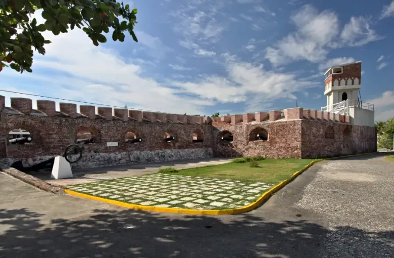 Historic brick fort in Jamaica with cannons mounted in arched embrasures crenellated walls and a white lighthouse tower
