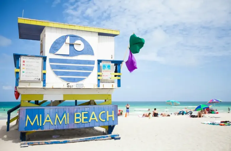 Colorful Miami Beach lifeguard station at 5th Street with green and purple warning flags flying on a sunny day.