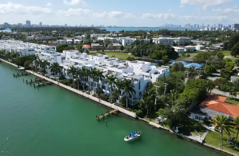 Aerial view of white modern waterfront condos along Miami Florida's Biscayne Bay with downtown skyline in background.