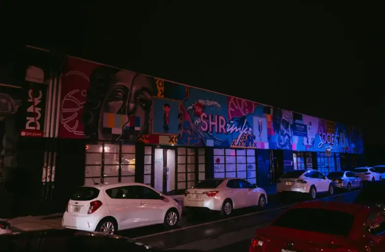 Colorful street murals illuminate a building facade at night in Miami; Florida's Wynwood arts district; with cars parked o