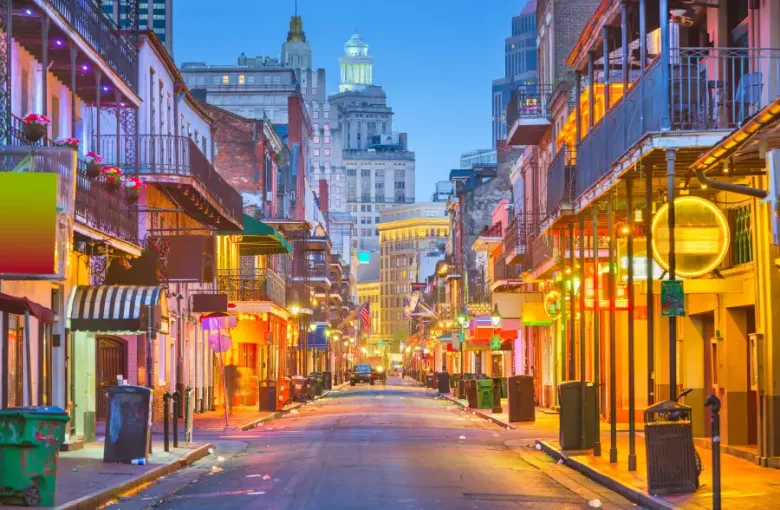 Bourbon Street in New Orleans Louisiana glows with colorful neon lights and iron-lace balconies at dusk with the city skyline beyond