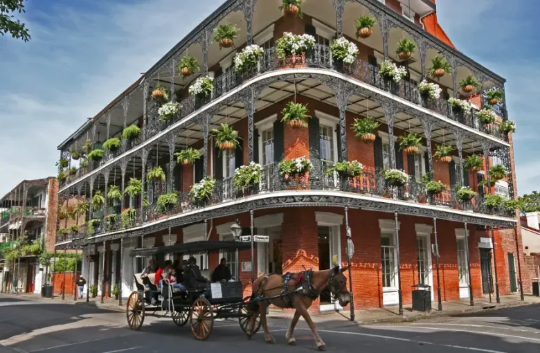 Horse-drawn carriage passes ornate iron-lace balconied brick building at Royal and Dumaine streets in New Orleans Louisiana