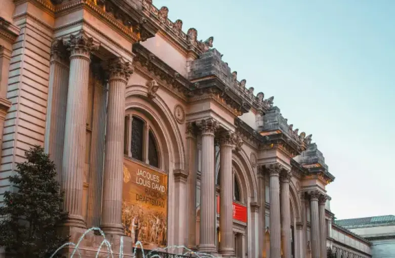 Metropolitan Museum of Art facade in New York New York with fountain at David H. Koch Plaza at dusk and Jacques-Louis David exhibition banner