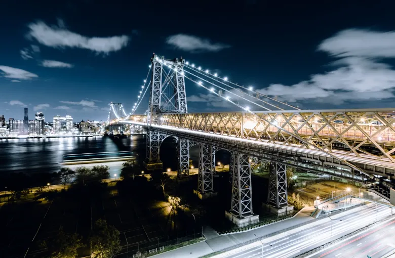Williamsburg Bridge illuminated at night over the East River with the New York New York Manhattan skyline glowing in the background