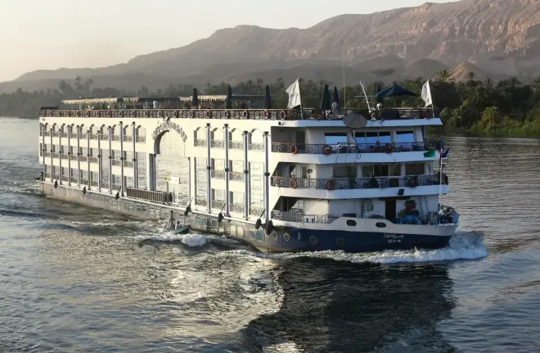 Large cruise-land riverboat sailing the Nile with desert cliffs and palm trees in the background; Egypt.