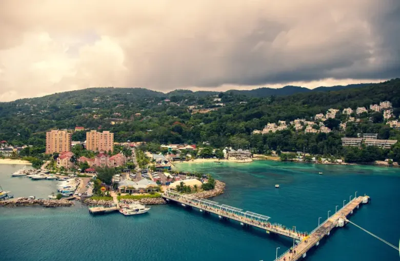 Aerial view of Ocho Rios Jamaica cruise port with turquoise bay pier marina and lush hillside town under stormy skies