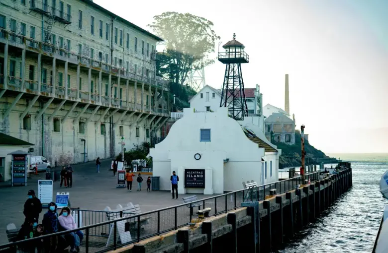 Visitors at Alcatraz Island dock in San Francisco; CA; with historic prison building and watch tower in background.