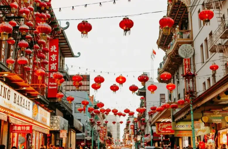 Red lanterns line Grant Avenue in San Francisco; CA's Chinatown; with shops and pedestrians along a vibrant street at dusk.