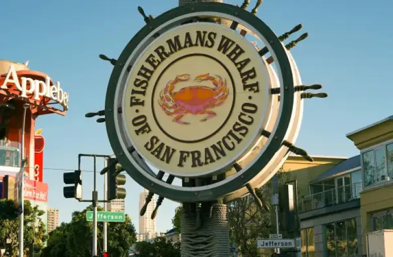 Iconic Fisherman's Wharf ship-wheel sign with crab emblem on Jefferson Street in San Francisco; CA; surrounded by visitors.