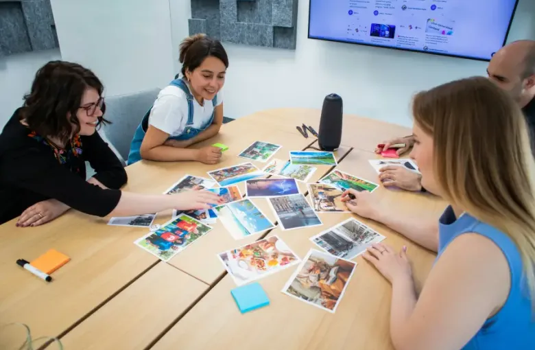 Four colleagues reviewing printed travel photos on a conference table during a travel-support planning session in a modern
