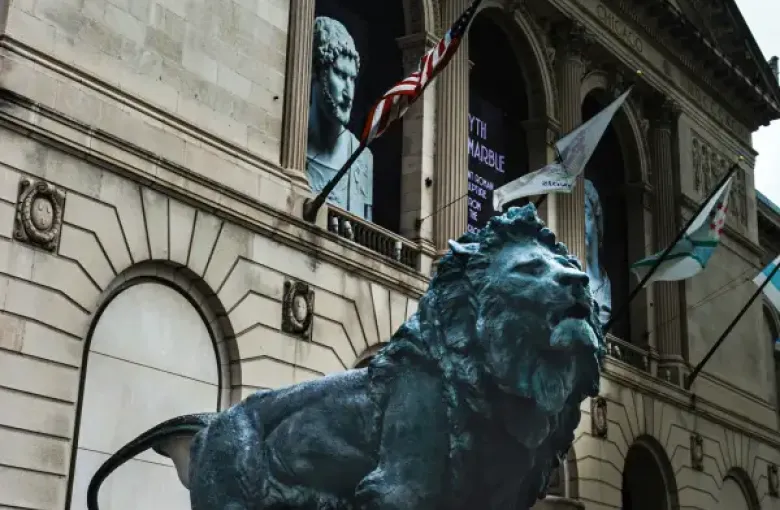 Bronze lion statue guards the entrance of the Art Institute of Chicago; with American and city flags visible behind it.