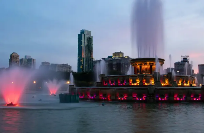 Buckingham Fountain illuminated with pink and gold lights at dusk; with Chicago's skyline visible in the background.