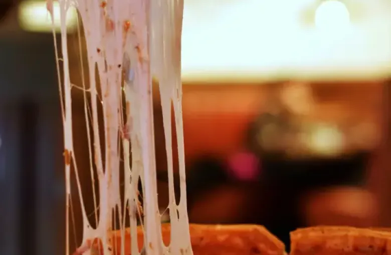 A slice of Chicago deep-dish pizza being lifted; stretching long strands of melted mozzarella from the pan below.