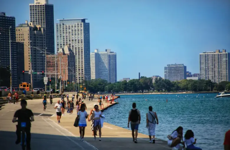 Pedestrians and cyclists enjoy Chicago's Lakefront Trail with Lake Michigan and the city skyline on a sunny summer day.