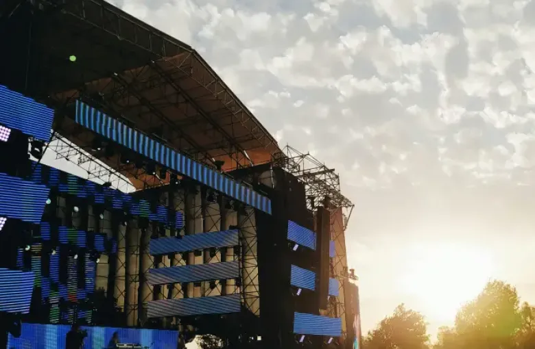 Large crowd at a Chicago outdoor music festival at sunset; with LED stage screens and a rainbow pride flag visible.