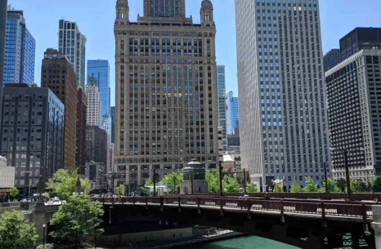 Packed tour boat on the turquoise Chicago River passes under a bridge with the Jewelers Building and Kemper tower beyond.