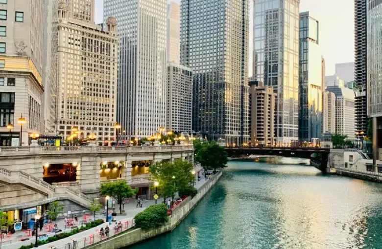 Chicago River Riverwalk with teal water; pedestrian promenade; and gleaming downtown skyscrapers at golden hour.