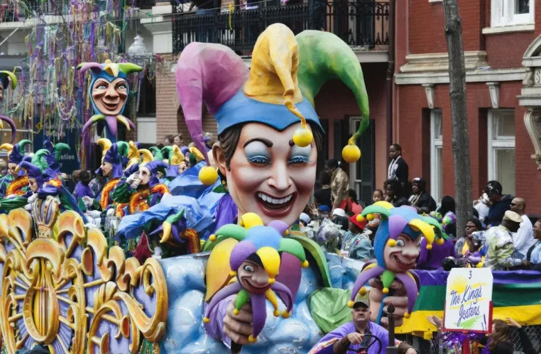 A colorful Mardi Gras parade float with a giant jester and costumed riders in purple, green, and gold in New Orleans