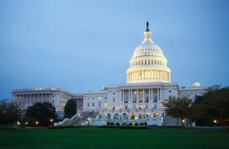The illuminated U.S. Capitol Building in Washington; DC glows at dusk against a blue twilight sky with manicured grounds.