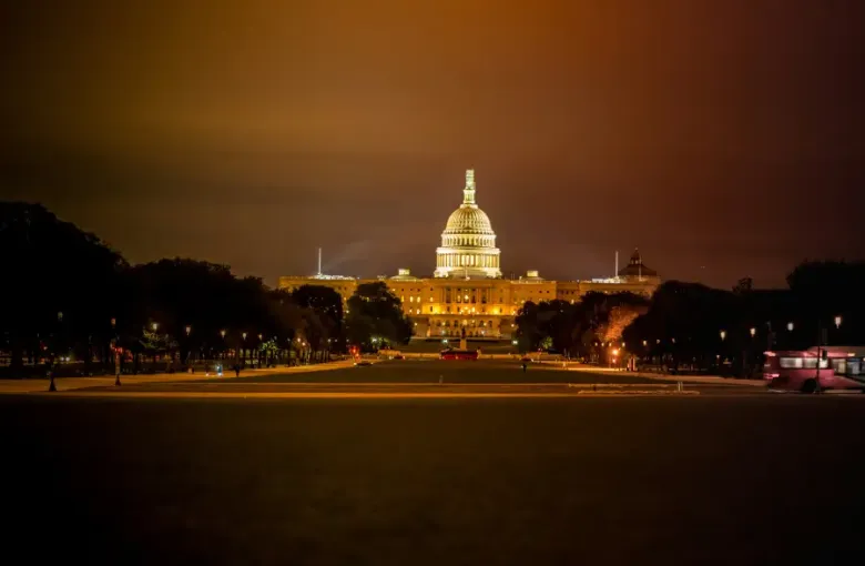 U.S. Capitol building glowing golden at night in Washington; DC; viewed from the National Mall with tree-lined paths.