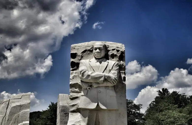 The Martin Luther King Jr. Memorial Stone of Hope sculpture in Washington DC; arms crossed; against a dramatic blue sky.